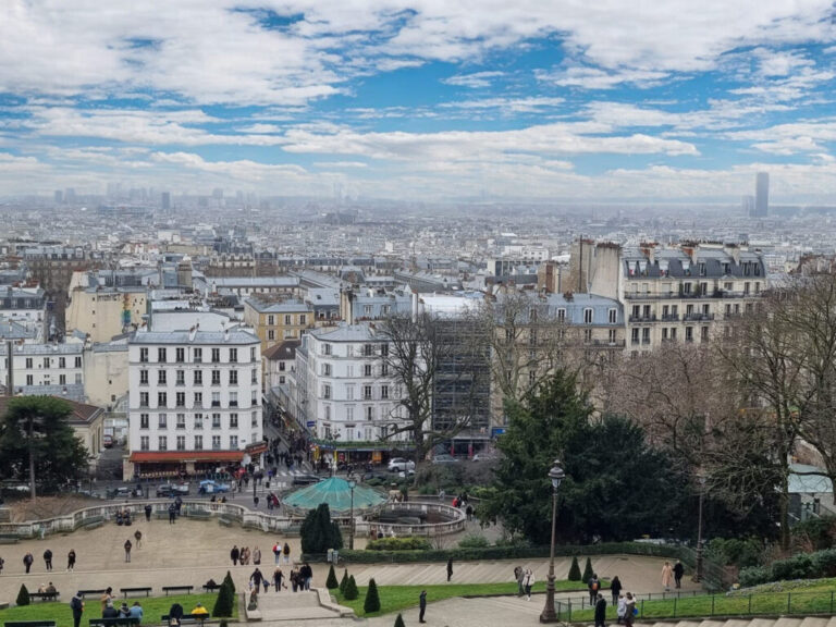 A panoramic view of Paris from the steps of Montmartre, with vibrant greenery and classic Parisian rooftops under a bright sky. A lively spot for families to explore without spending a dime.