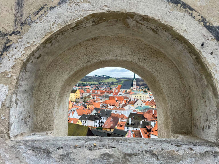 A view of Cesky Krumlov’s colorful rooftops and distant church tower, framed perfectly through a small arched stone window. This hidden perspective is one of many charming sights discovered on a free walking tour in Cesky Krumlov.