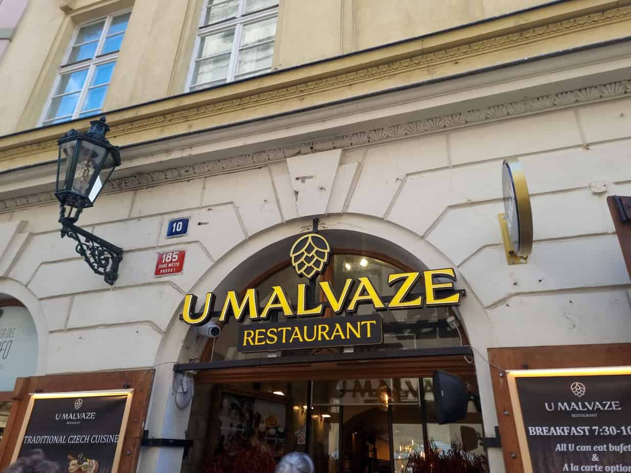 Entrance to U Malvaze Restaurant, with a bold gold-lettered sign, lantern, and signage offering traditional Czech cuisine and breakfast options.