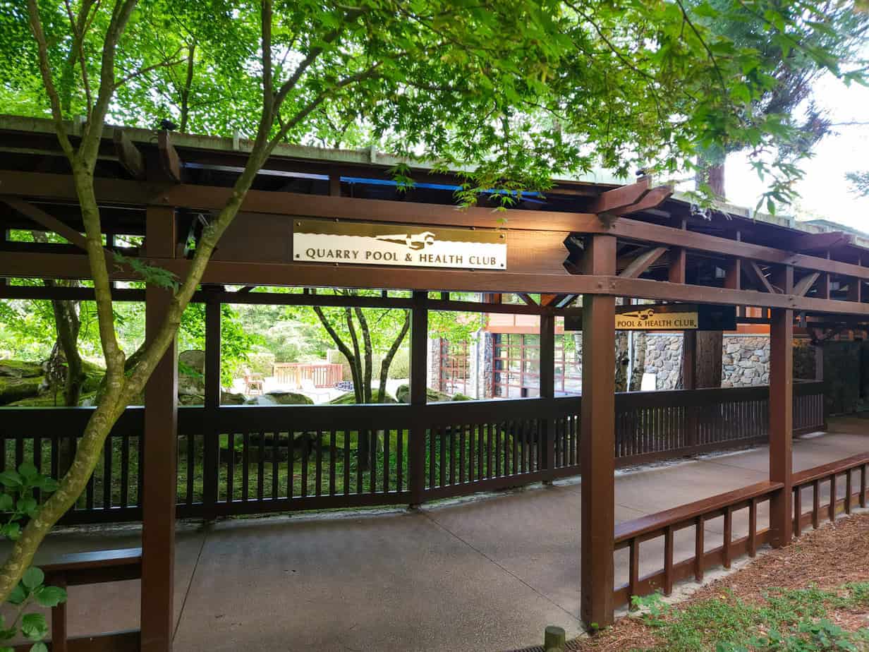 Covered wooden walkway to the Quarry Pool & Health Club, surrounded by dense greenery, leading to a wellness area likely part of Sequoia Lodge.