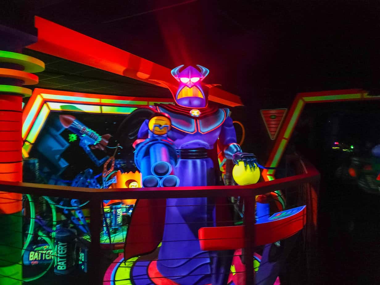 A glowing figure of Emperor Zurg looms in blacklight, surrounded by futuristic props on the Buzz Lightyear ride in Disneyland Paris.