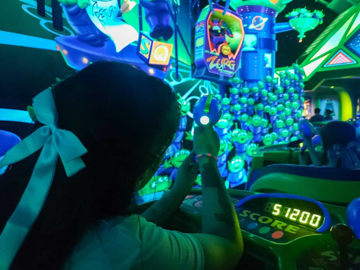 A guest aims a laser gun while riding Buzz Lightyear Laser Blast, with glowing targets and a score display showing 51200.