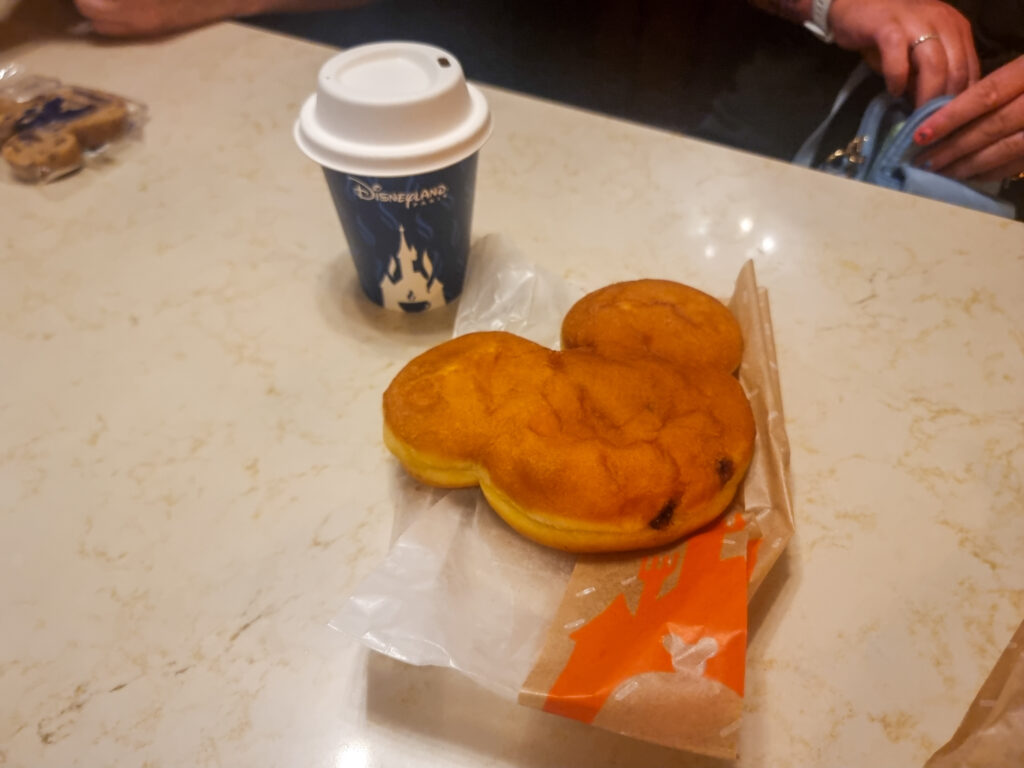 A Mickey-shaped filled brioche and a hot coffee in a Disneyland Paris cup on a table—iconic park breakfast combo.