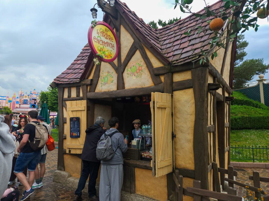 Guests line up at Maurice’s Popcorn, a charming Tudor-style snack stand with wooden shutters and a sign inspired by Beauty and the Beast.