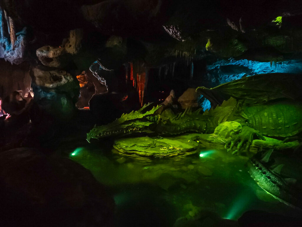 Inside a dimly lit cave beneath Sleeping Beauty’s Castle lies a large animatronic dragon resting beside glowing green water. This unique walkthrough is part of the Disneyland Paris rides and attractions list.