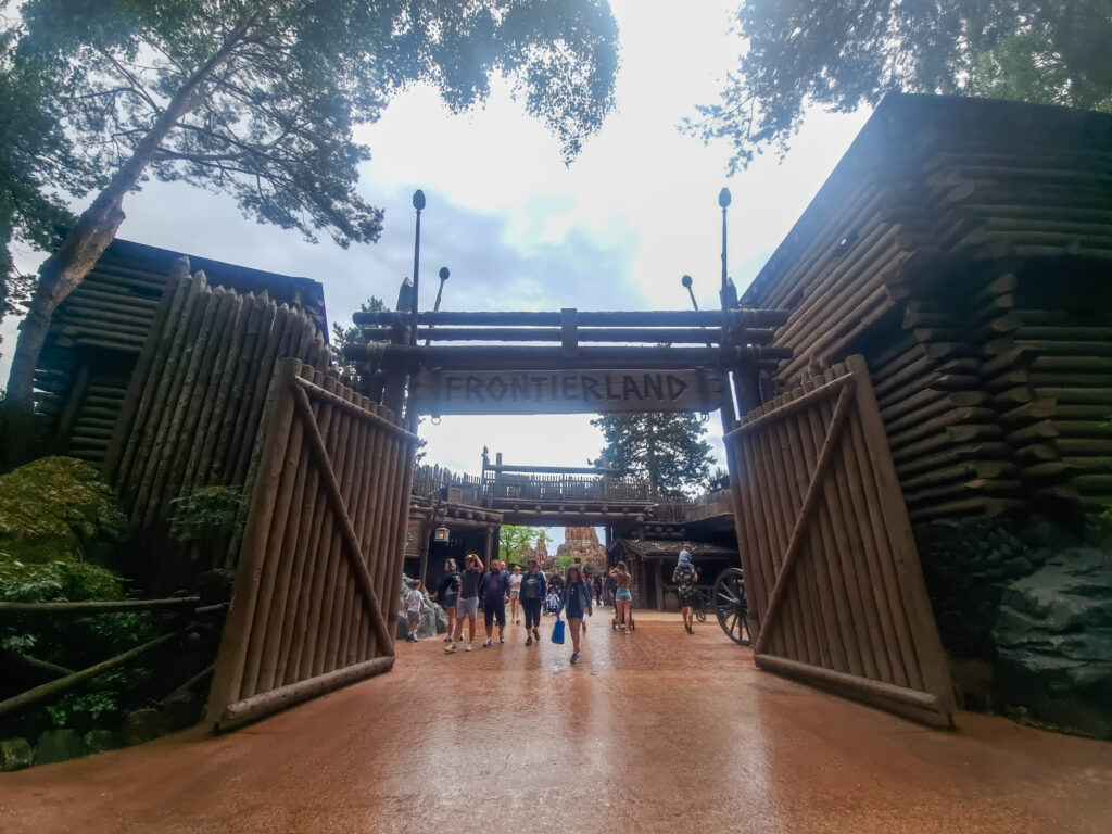 Large wooden gates welcome guests into Frontierland, styled like an Old West fort with log walls and rustic lanterns. Featured in the Disneyland Paris rides and attractions list.