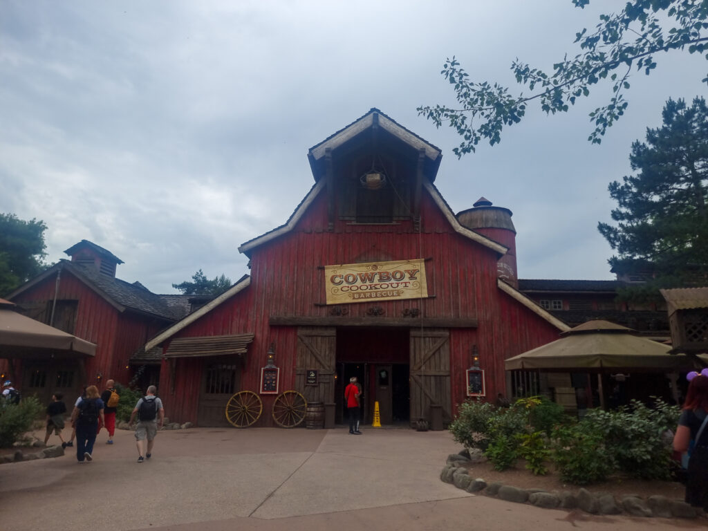 A large red barn-themed building marked “Cowboy Cookout Barbecue” stands in Frontierland, inviting guests into a Western-style dining experience.