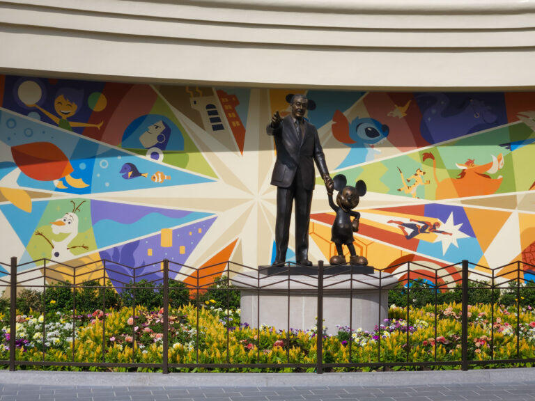 The famous Partners Statue of Walt Disney holding Mickey Mouse’s hand stands in front of a vibrant mural featuring beloved Disney and Pixar characters.
