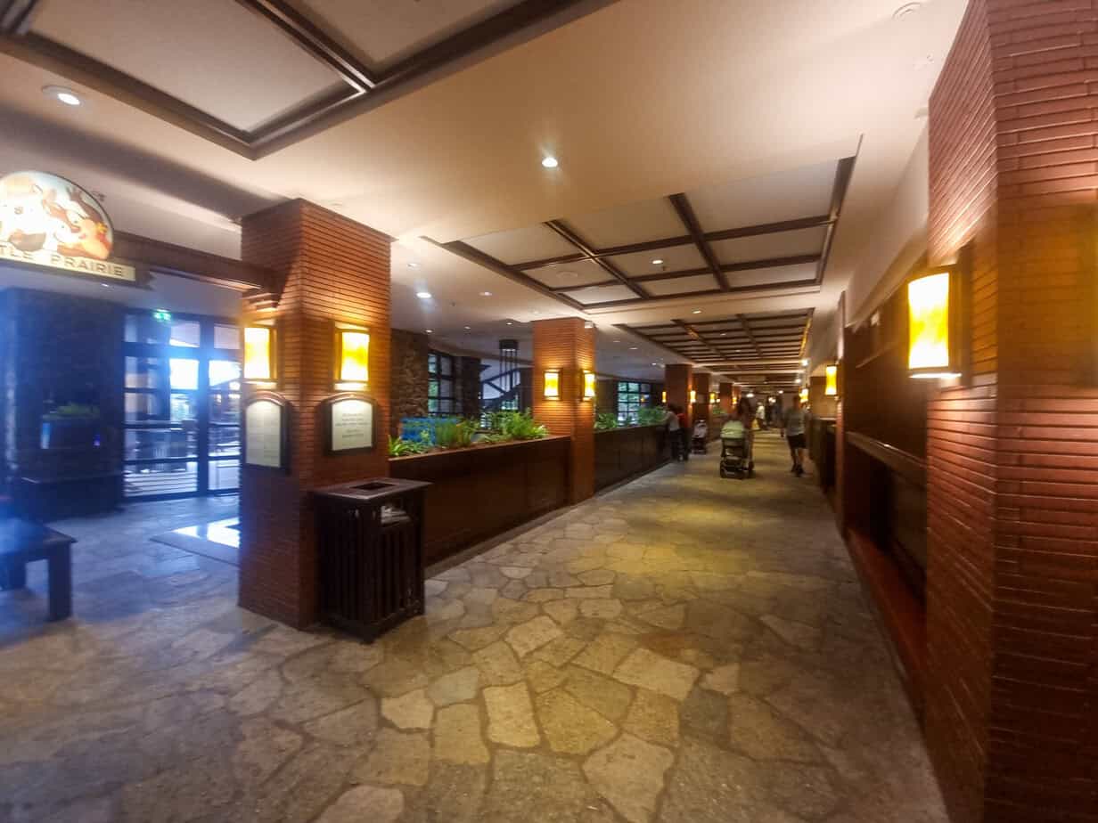 Interior corridor at Disney’s Sequoia Lodge with stone flooring, warm wood paneling, and ambient lighting, leading to restaurants and other guest amenities.