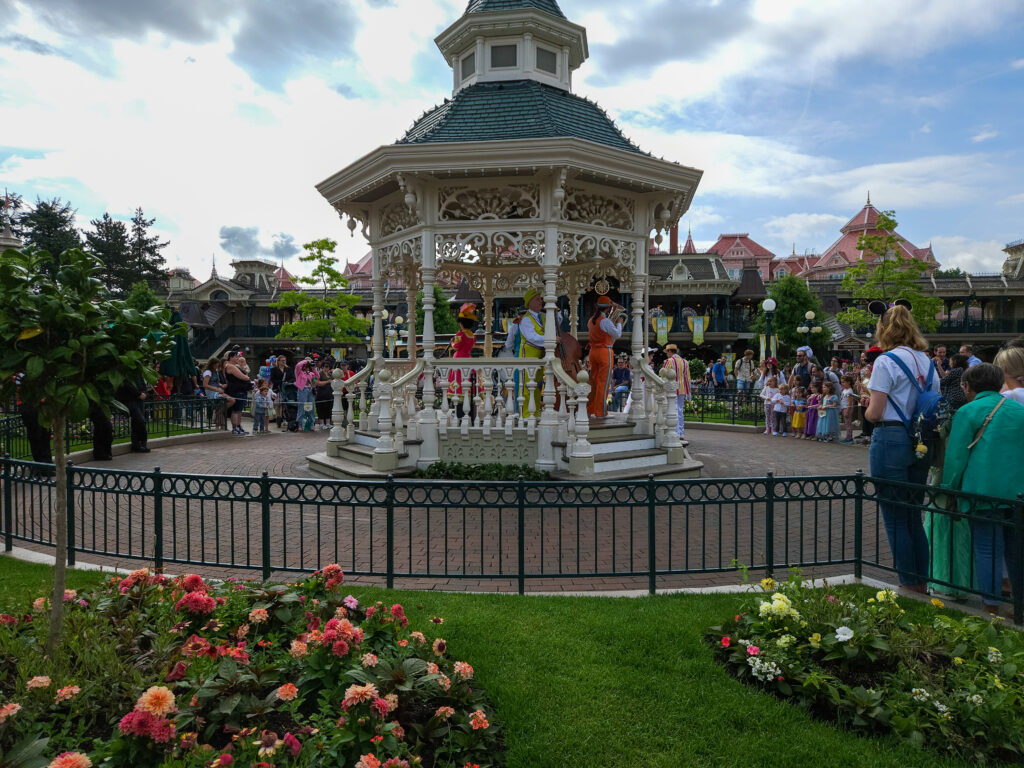 Guests line up around a white gazebo surrounded by flowerbeds for a character meet-and-greet at the Town Square Gardens.