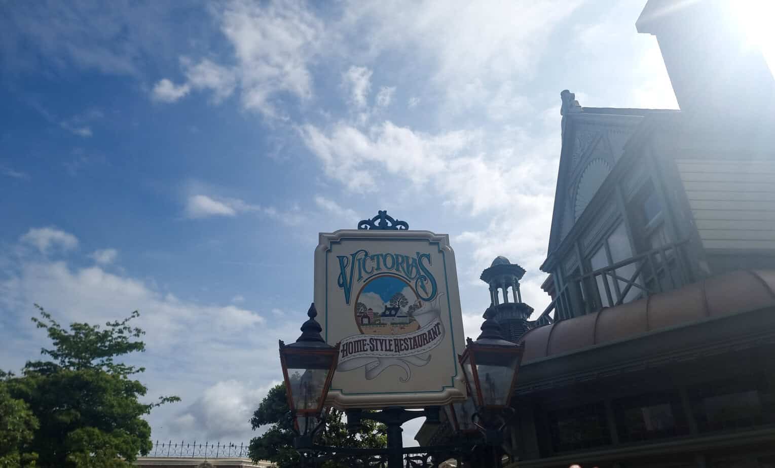 The Victorian-style exterior sign of Victoria’s Home-Style Restaurant at Disneyland Paris, with cloudy blue skies behind it.