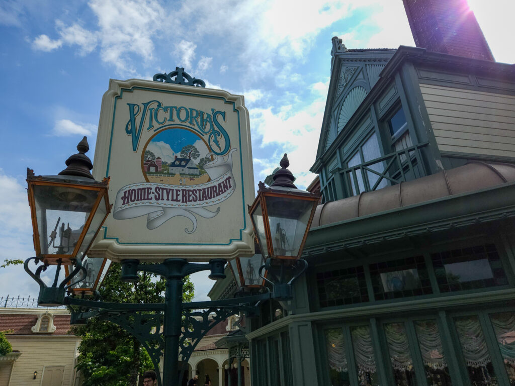 An ornate vintage sign for Victoria’s Home-Style Restaurant hangs between two gas-style lanterns, set against the classic green trim of the Main Street building.