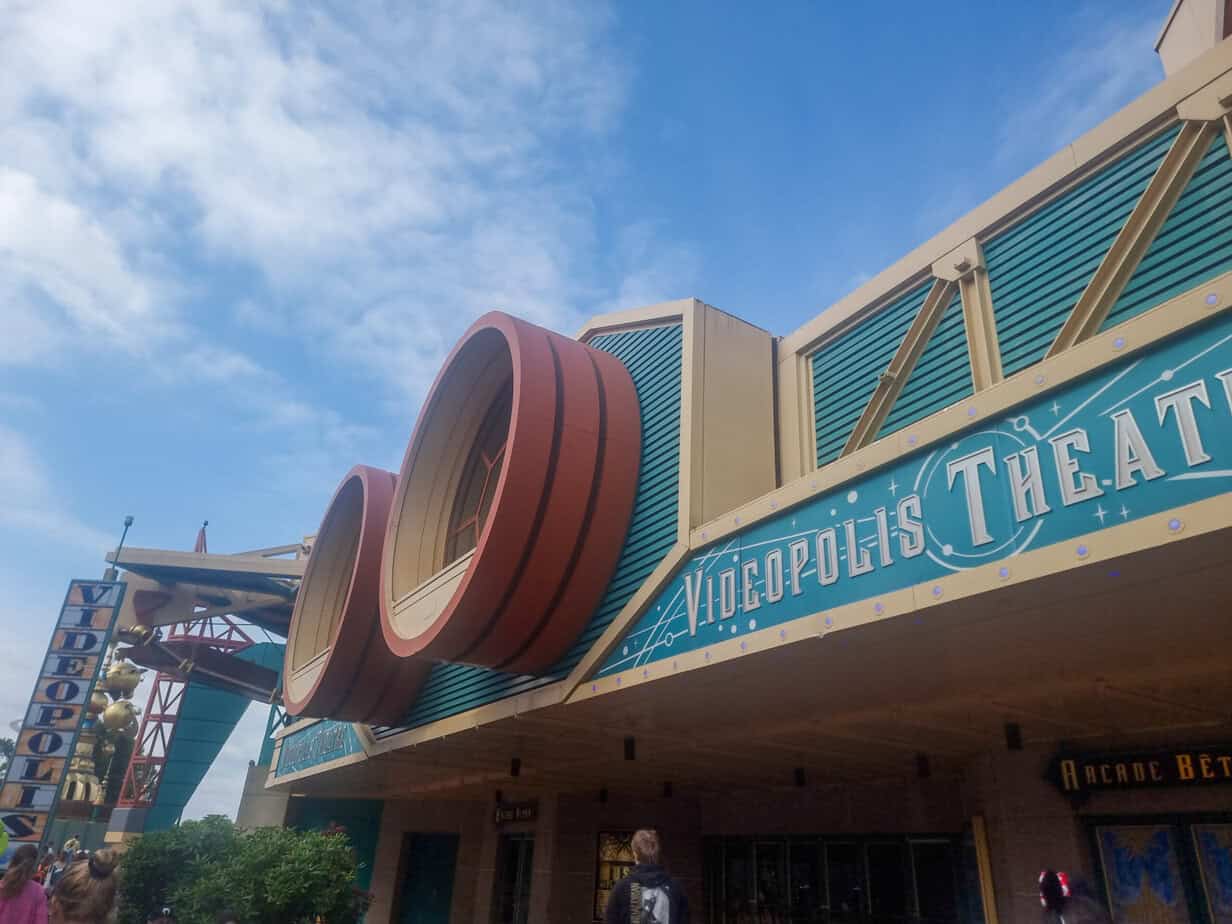 The bold, retro facade of Videopolis Theatre stands under a sunny sky, its teal and red Art Deco-style entrance drawing attention.