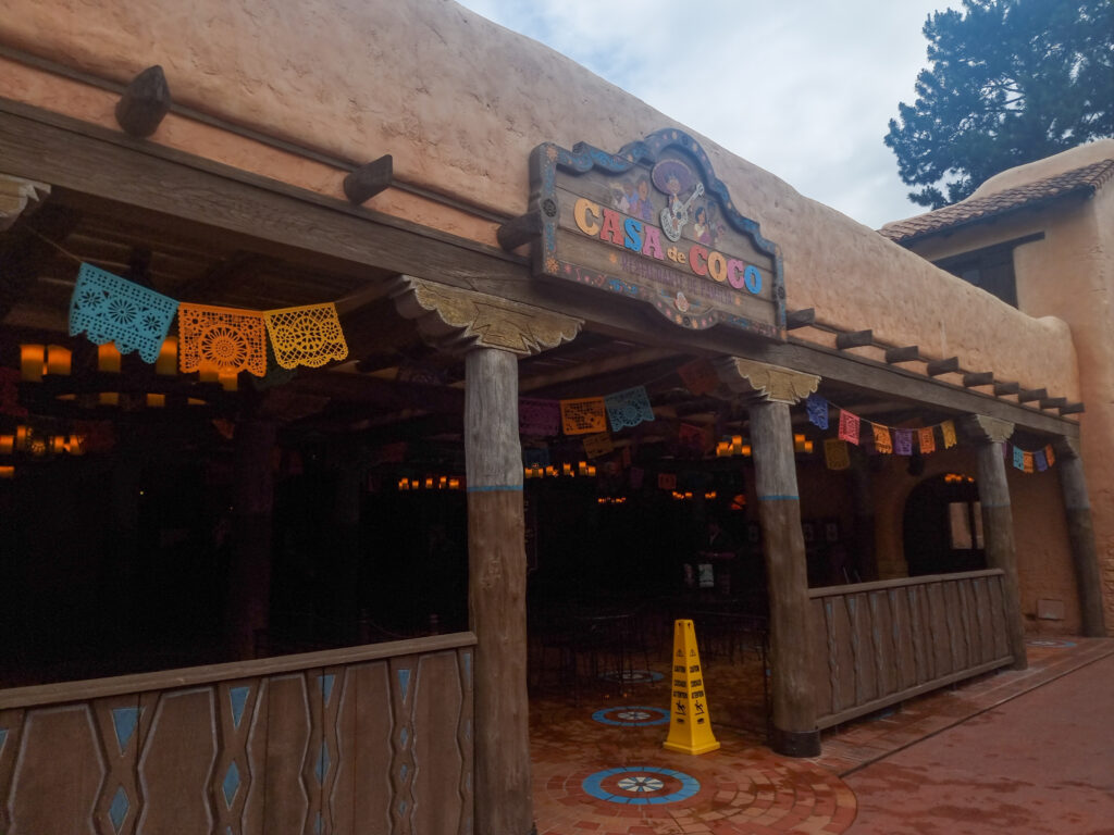 The warmly lit exterior of Casa de Coco, a Mexican-themed dining area decorated with papel picado banners and wooden columns.