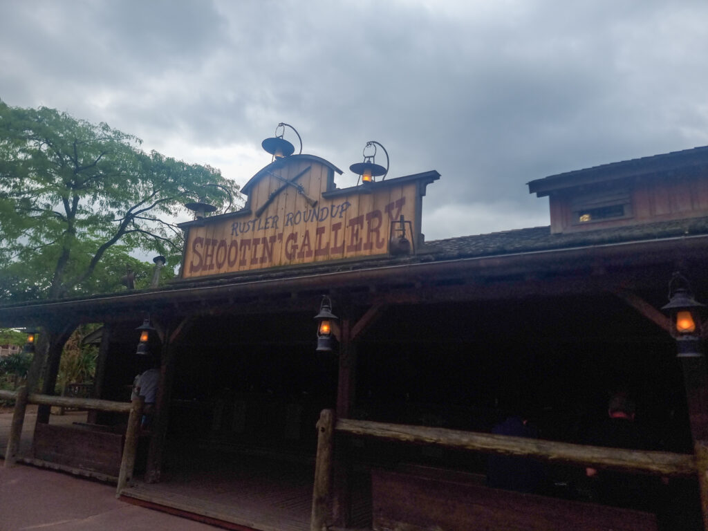 Wooden signage for the Shootin’ Gallery rests above a covered Western-style porch, complete with lanterns and wooden fencing.