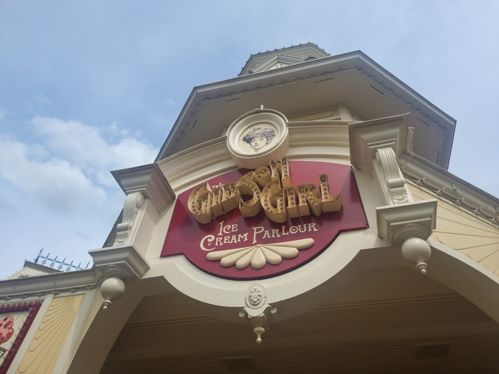 A red-and-cream sign for The Gibson Girl Ice Cream Parlour is mounted under a vintage-style clock tower with decorative trim.