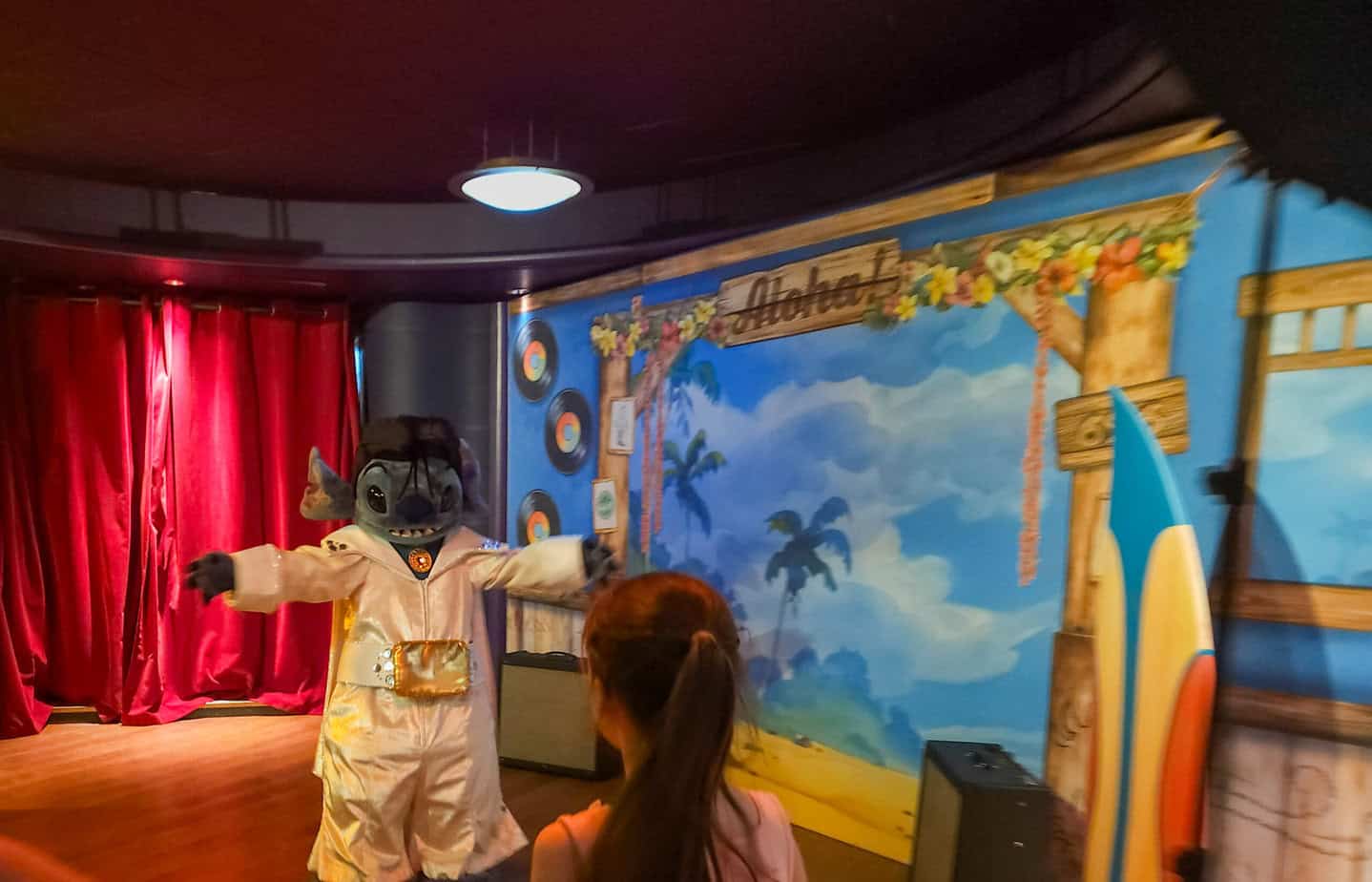 A child approaches Stitch dressed as Elvis in front of a colorful tropical backdrop reading "Aloha!" — one of the lesser-known disneyland paris secrets.