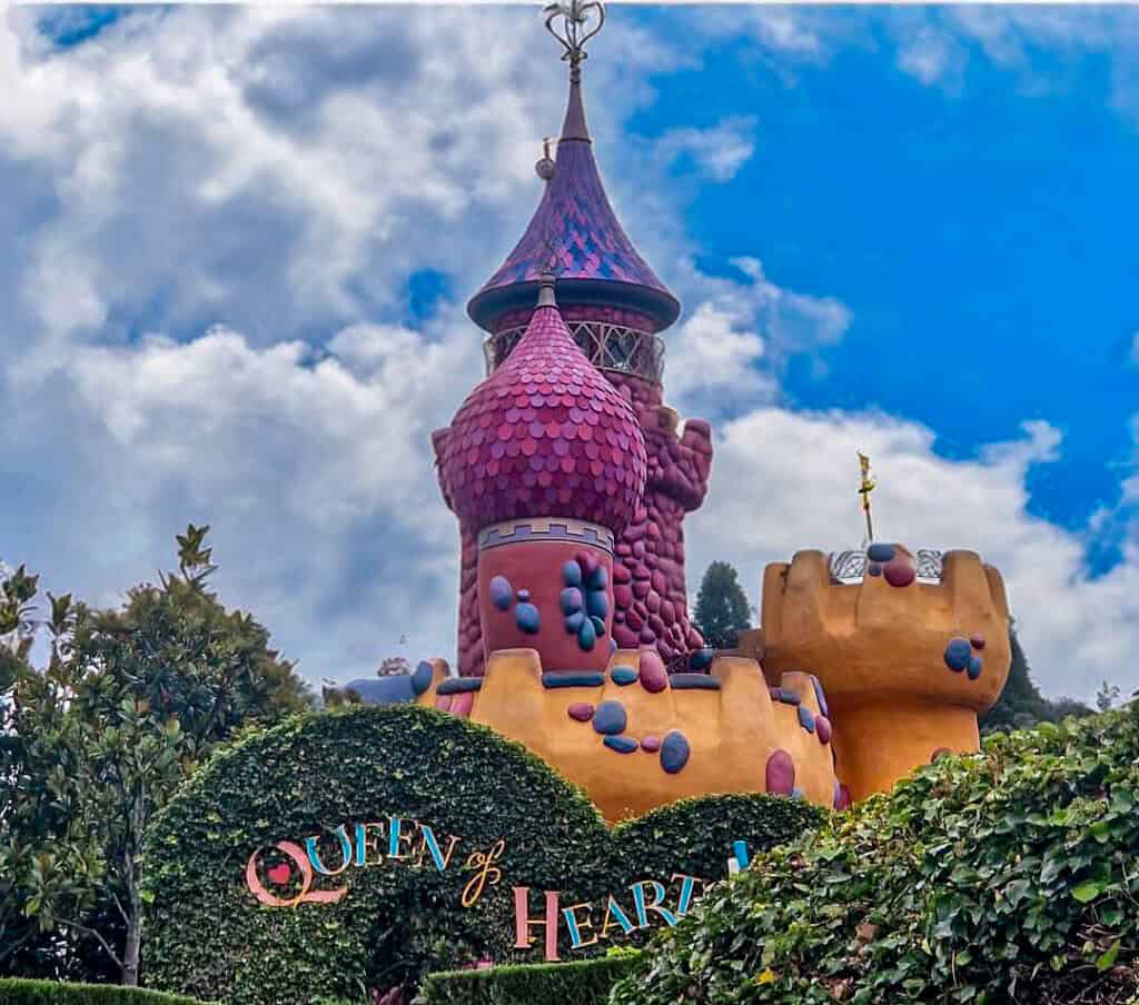 A whimsical purple and red tower peeks above a hedge maze entrance marked “Queen of Hearts,” styled with colorful fantasy architecture from Alice in Wonderland. Included in the Disneyland Paris rides and attractions list.
