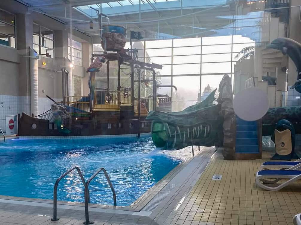 Indoor aquatic play area at the Explorers Hotel featuring a pirate-themed ship, dragon water slide, and blue swimming pool—one of several disneyland paris hotels with pools perfect for kids.