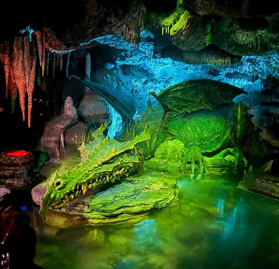 A fearsome green dragon lies asleep in a dark, misty cavern lit with eerie blues and greens — one of the most unexpected disneyland paris secrets beneath Sleeping Beauty Castle.