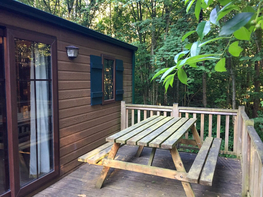 Private wooden cabin patio in the woods with a picnic table, giving off a peaceful, nature-immersed retreat vibe.