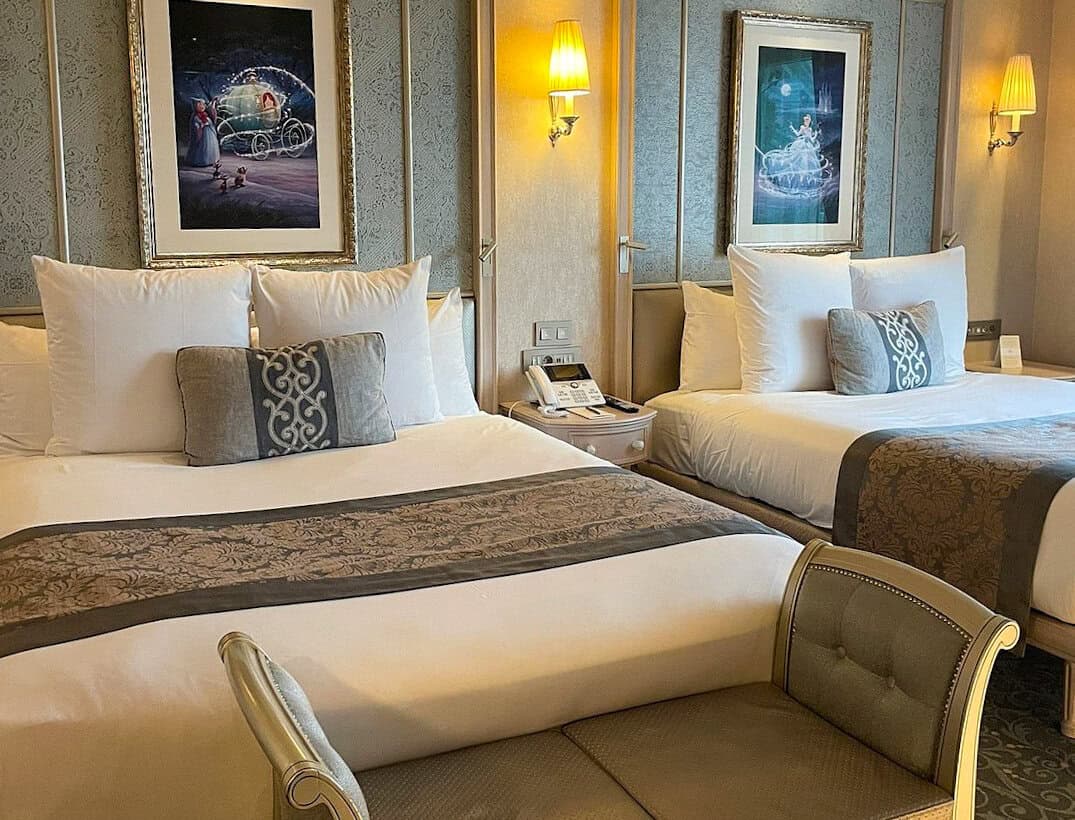 Charming and luxurious hotel room with two double beds, royal blue and gold accents, and framed Cinderella-themed artwork on the wall.