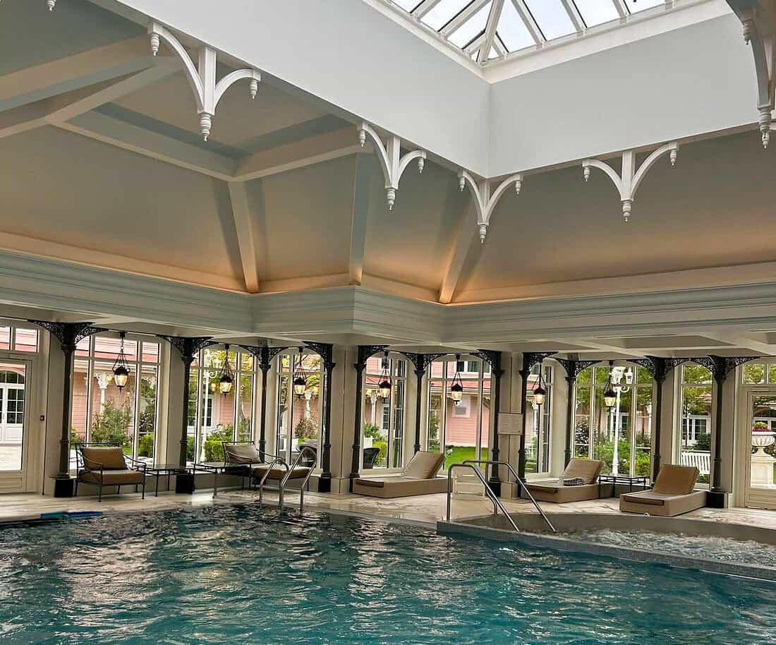 Elegant indoor pool under a vaulted glass ceiling with decorative beams and lounge seating, exemplifying the upscale appeal of disneyland paris hotels with pools.