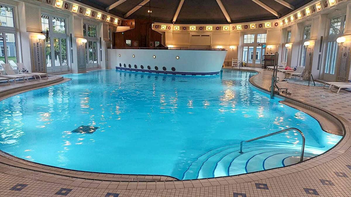 Nautical-themed indoor pool with a mock ship structure in the center, surrounded by deck chairs and decorative tile flooring, showcasing the charm of disneyland paris hotels with pools.