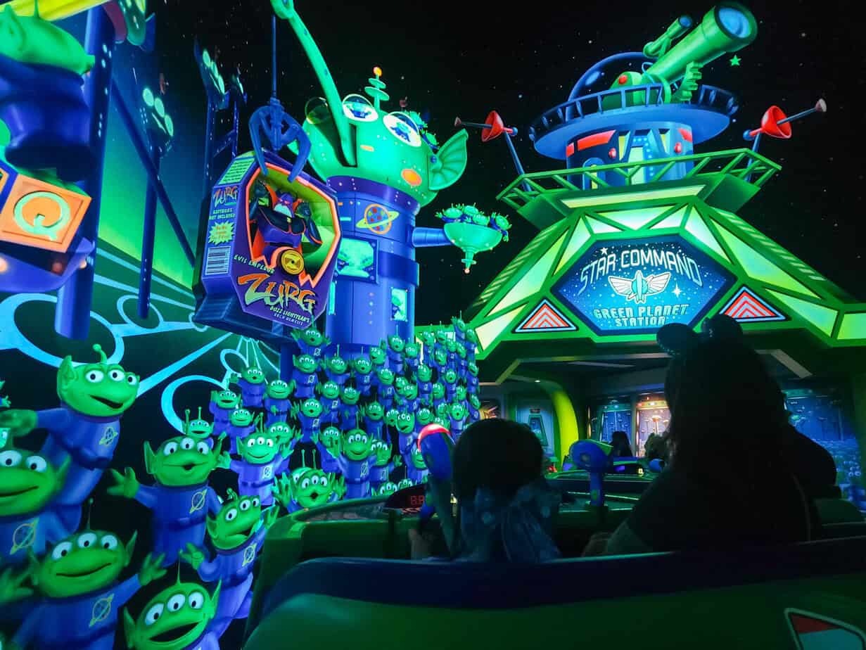 An indoor Toy Story Buzz Lightyear ride scene at Disneyland Paris with neon-lit aliens, a claw machine, and Star Command headquarters, where guests aim laser blasters at targets.