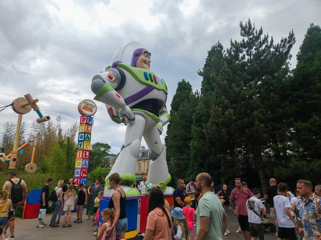 Crowds gather around a towering statue of Buzz Lightyear at the entrance to Toy Story Playland, an essential part of the Disneyland Paris Toy Story experience with building block signs and playful props.