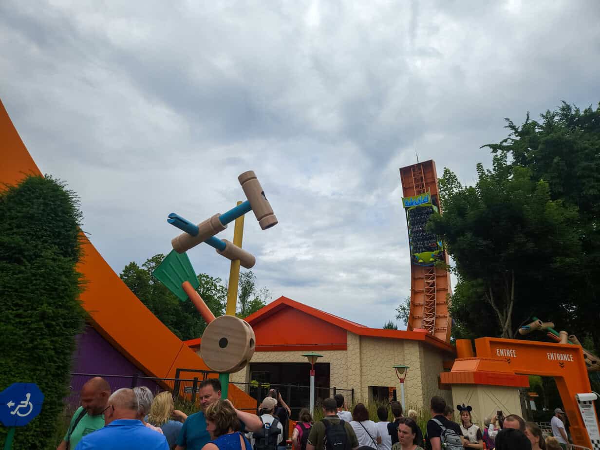 Guests queue outside a bright orange and cream building at Disneyland Paris, leading to RC Racer, a high-speed ride shaped like a Hot Wheels track loop.