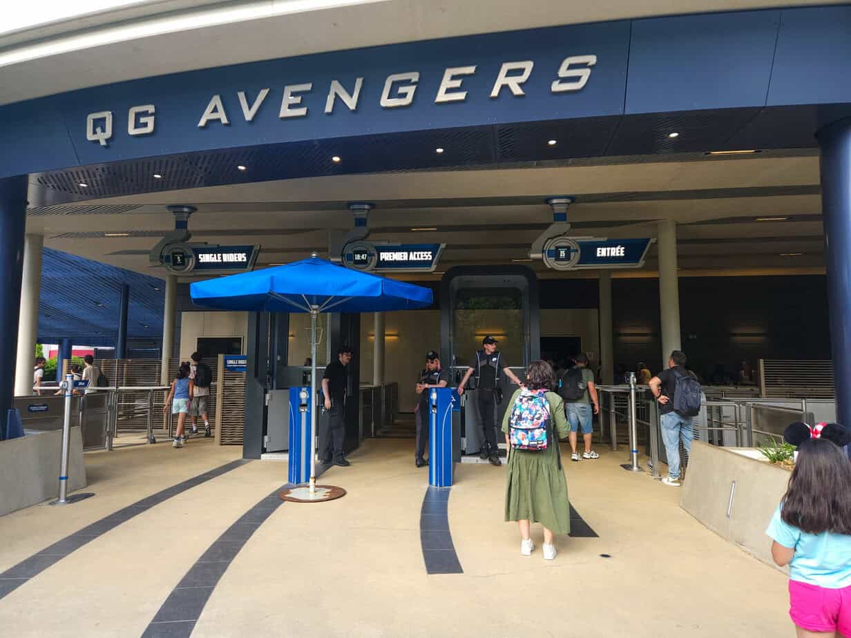 Visitors approach the QG Avengers entrance at Disneyland Paris, a modern structure with dark blue signage and lanes for regular, Premier Access, and single riders.