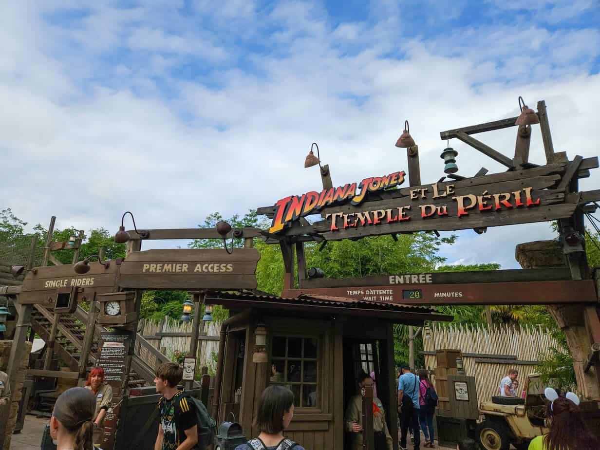The rustic, jungle-themed entrance to Indiana Jones et le Temple du Péril shows a 20-minute wait time and directional signs for single riders and Premier Access.