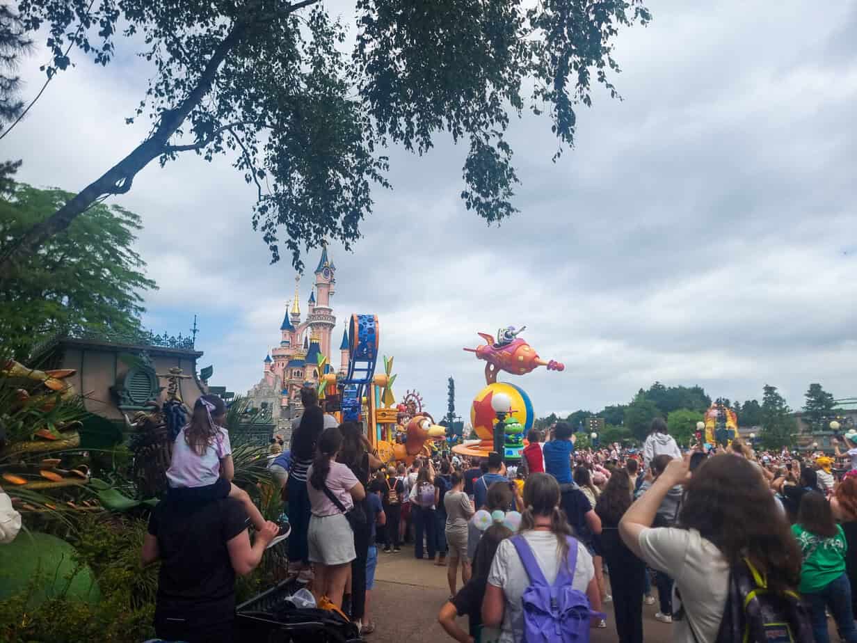 Disneyland Paris parade in front of Sleeping Beauty Castle, with crowds lining the street.