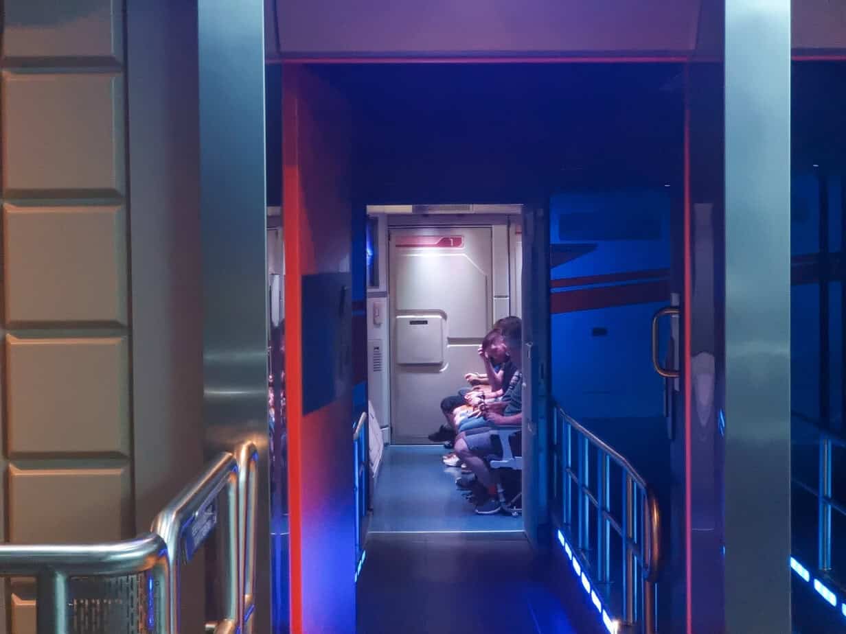 Guests are seated in rows inside the Star Tours shuttle cabin at Disneyland Paris Star Wars, moments before takeoff. The setting features glowing panels and a corridor styled like a transport vessel.