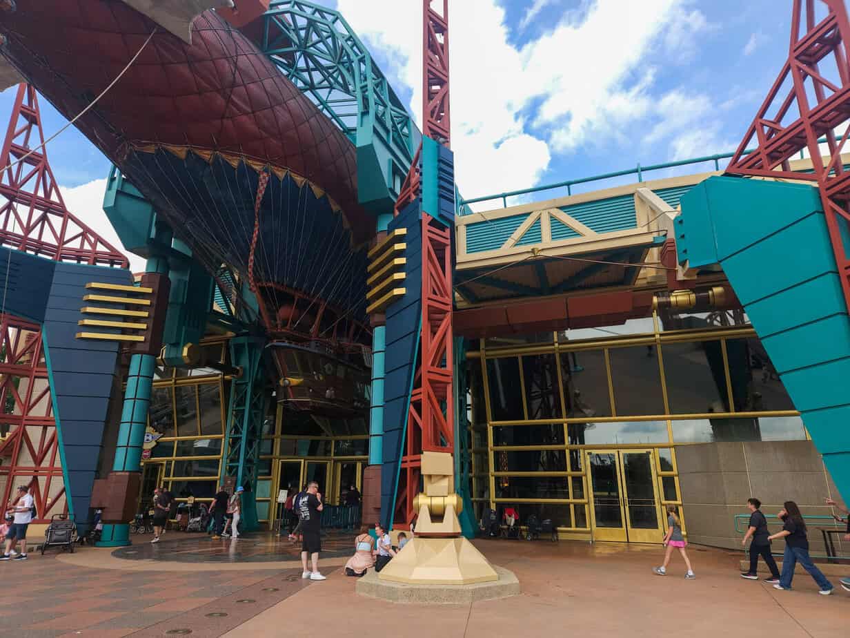 The angular, multicolored entrance to a sci-fi building at Disneyland Paris shows geometric teal, red, and gold structures towering above the plaza. Guests stroll beneath the futuristic overhang.