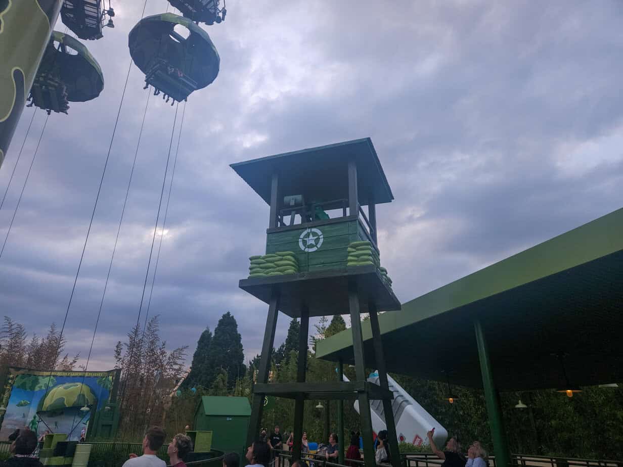 A tall green lookout tower and swinging parachute ride from the Toy Soldiers Parachute Drop attraction, capturing a dynamic moment in the Disneyland Paris Toy Story experience.