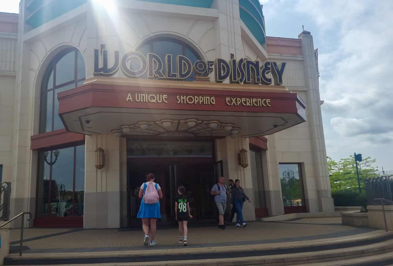Entrance to the World of Disney store at Disneyland Paris with art deco-inspired architecture and the tagline “A Unique Shopping Experience” above the door as guests walk in and out.