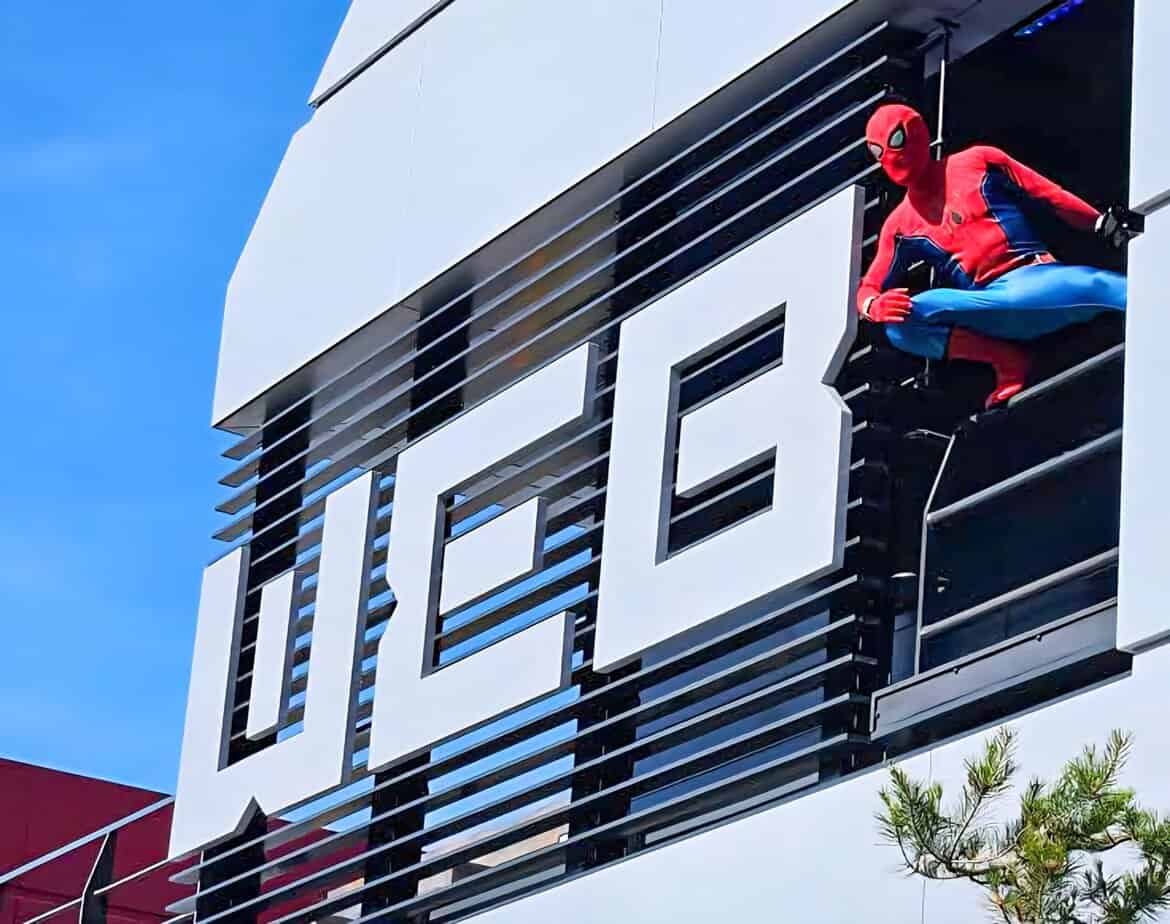 Spider-Man crouching on a ledge outside the W.E.B. Adventure building during a rooftop appearance at Disneyland Paris.