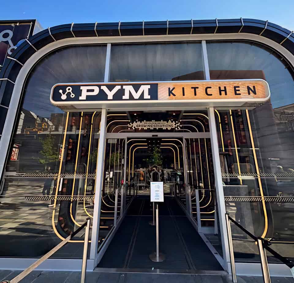 Front of Pym Kitchen buffet restaurant with themed shrinking tunnel-style entrance and modern glass facade.