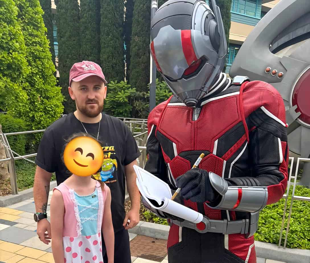 Ant-Man signing an autograph for a young girl while Callum stands next to them outside Avengers Campus.