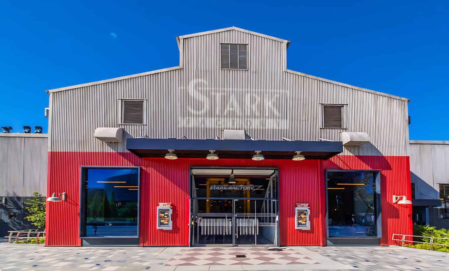 Entrance to Stark Factory quick-service restaurant with red and silver industrial-style building under a clear blue sky.