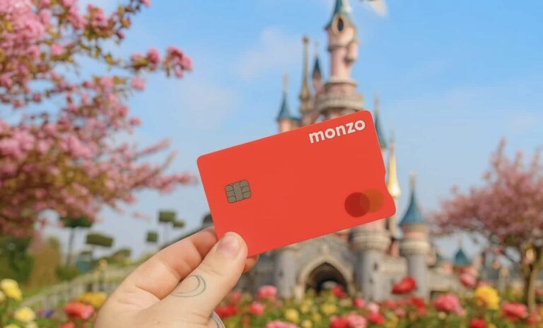 A person showcasing their bank card at Disneyland Paris, emphasizing the ease of using contactless payment while standing near blooming cherry trees and iconic castle turrets.