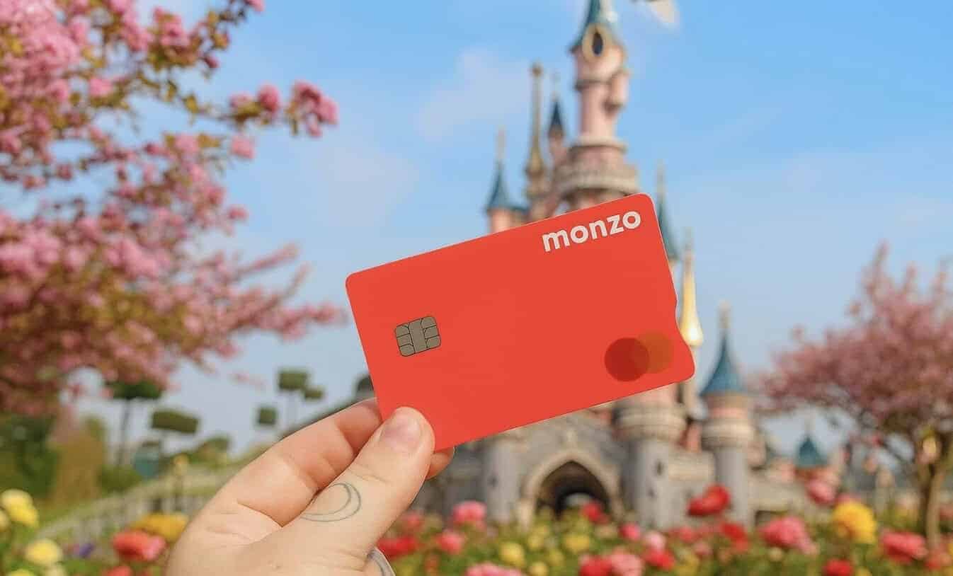 A person showcasing their bank card at Disneyland Paris, emphasizing the ease of using contactless payment while standing near blooming cherry trees and iconic castle turrets.