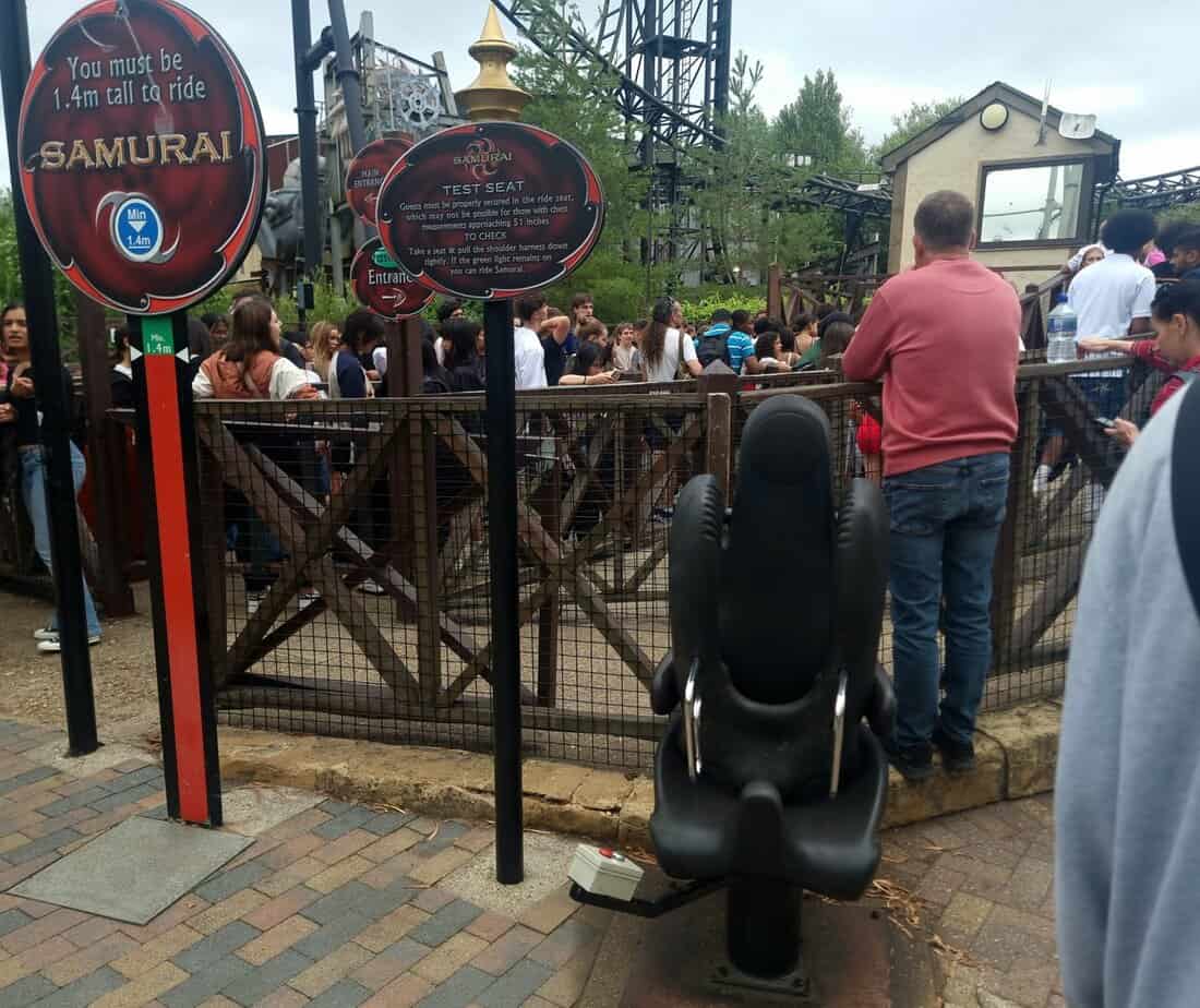 A black Samurai test seat sits near signs explaining the 1.4m minimum height requirement and chest measurement warning. This setup helps guests check comfort and fit, which is especially useful when navigating plus size at Thorpe Park.