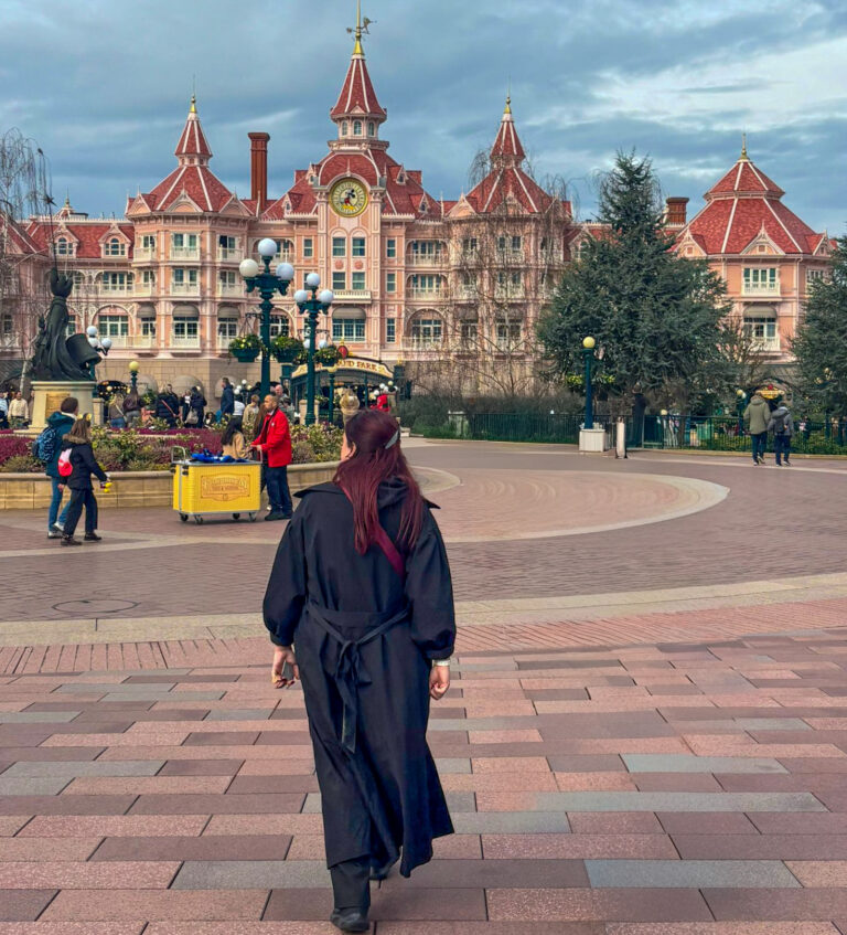 A person walks toward the Disneyland Hotel entrance with its pink Victorian style architecture and clock tower in view. The scene captures arrival excitement and raises the question is disneyland paris worth it on a paris trip.