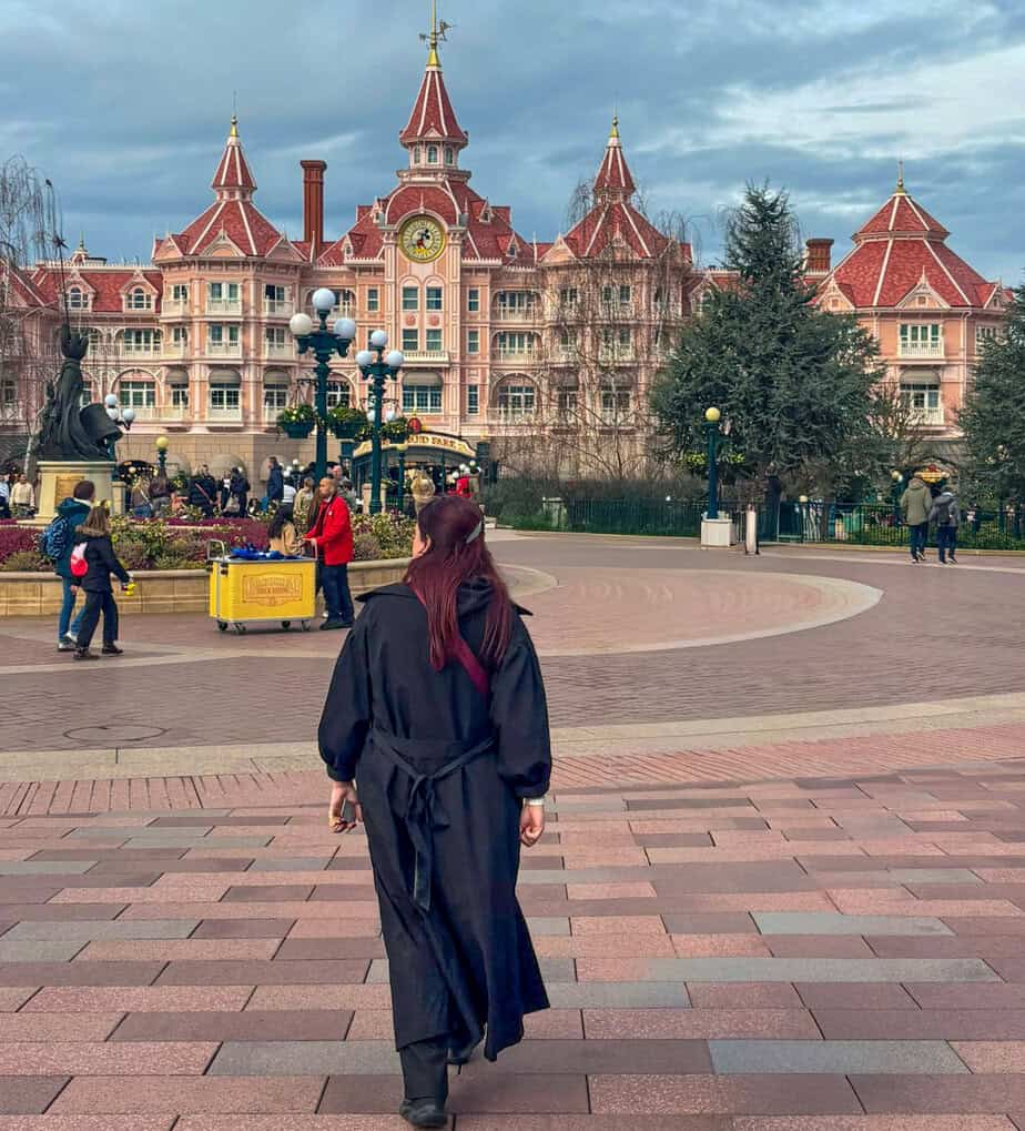 A person walks toward the Disneyland Hotel entrance with its pink Victorian style architecture and clock tower in view. The scene captures arrival excitement and raises the question is disneyland paris worth it on a paris trip.