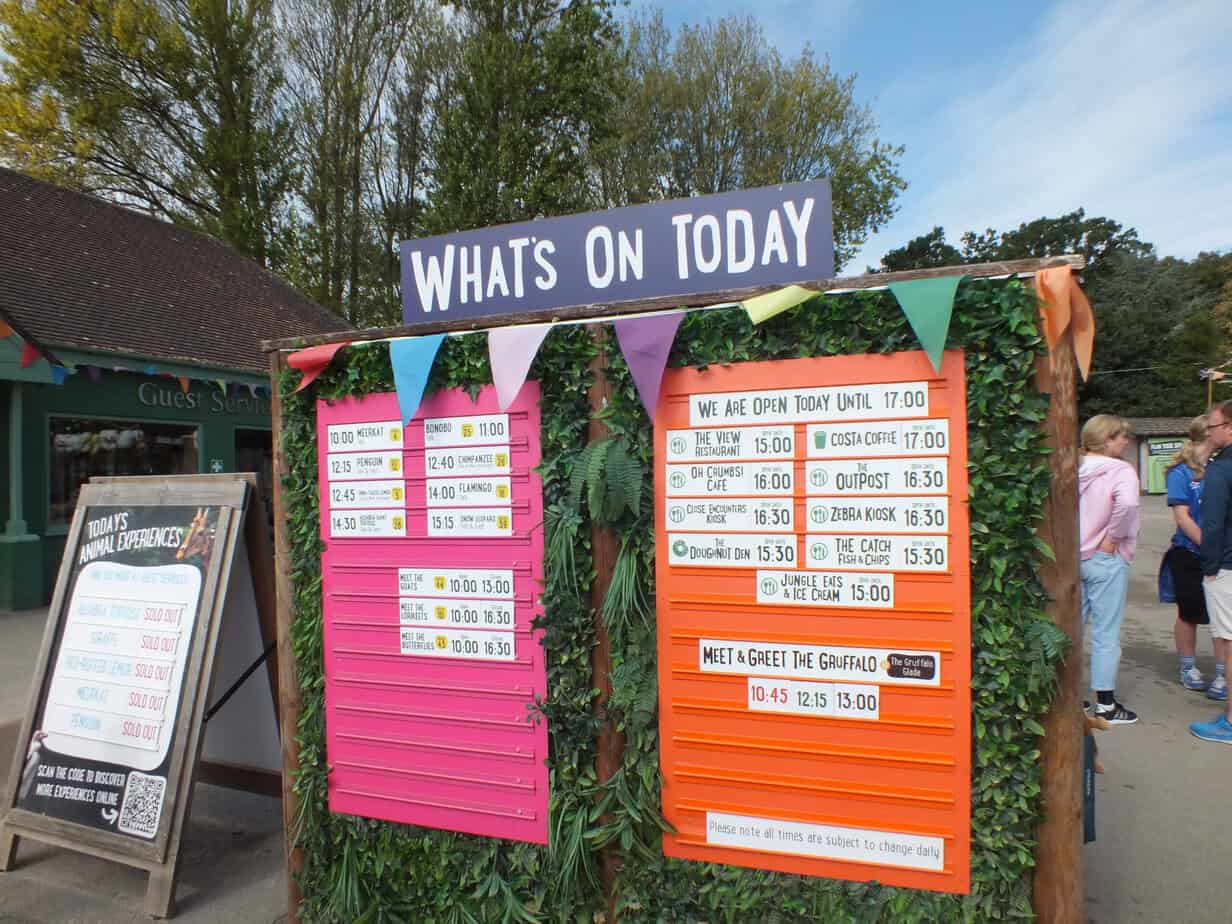 : Colourful information board at Twycross Zoo headed "WHATS ON TODAY". The board lists daily animal experiences opening times food outlets and "MEET AND GREET THE GRUFFALO" times of "10.45 12.15 13.00" helping families plan their visit and decide whether Twycross Zoo Worth It.
